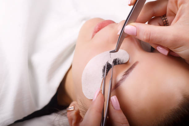 a photo showing a person's hands carefully installing lash extensions on a woman's lashes